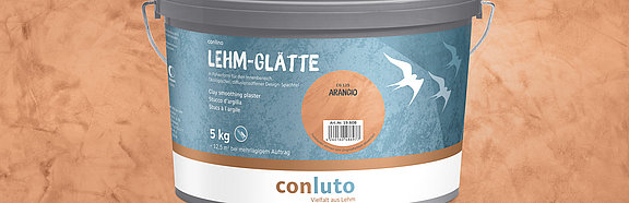 Lehm-Glätte Arancio conluto Lehm-Glätte im Eimer (Farbton Arancio) vor Wandausschnitt im selben Farbton