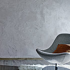 Holzhocker und grauer Sessel vor grauer Lehm-Edelputz Wand